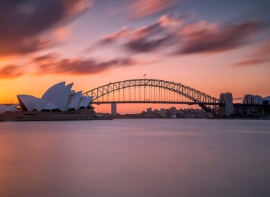 A beautiful shot of the Sydney harbor bridge with a light pink and blue sky in the background at sunset